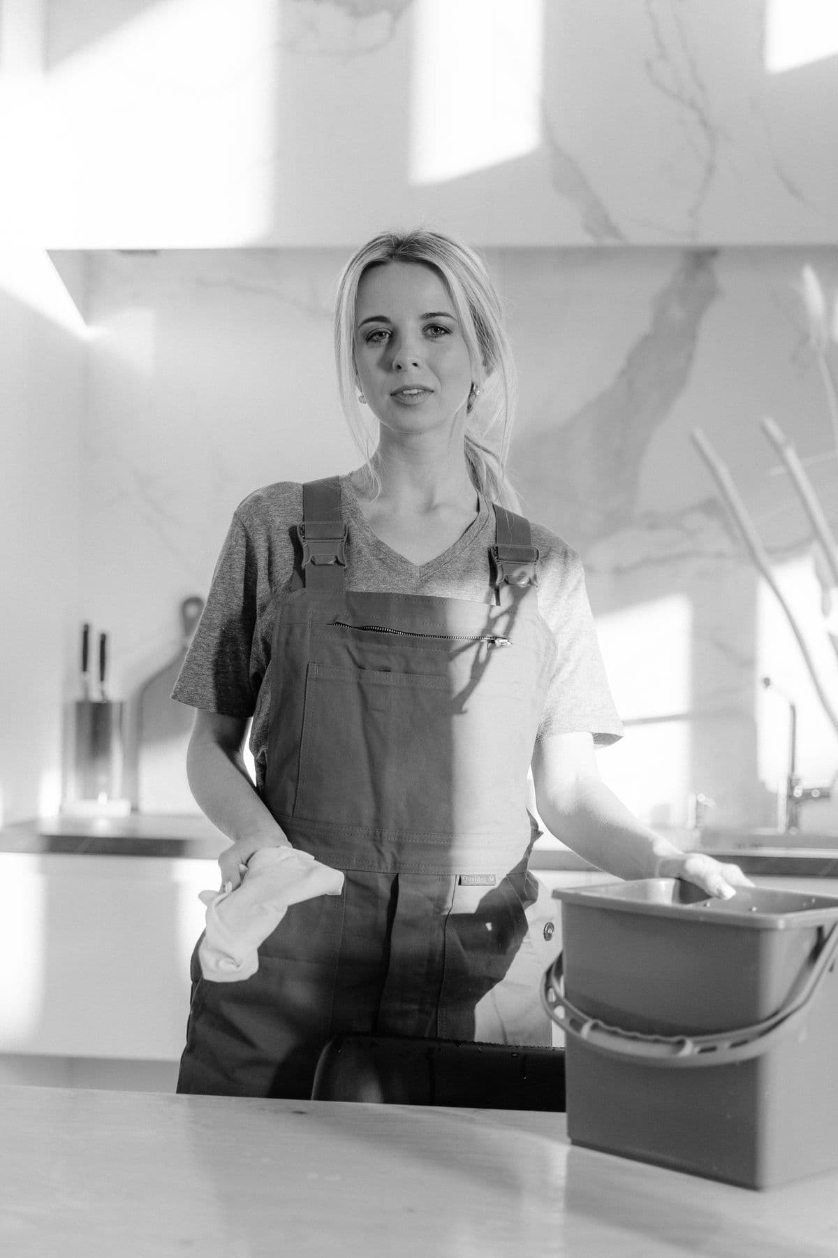 A person in overalls holding a bucket in a kitchen